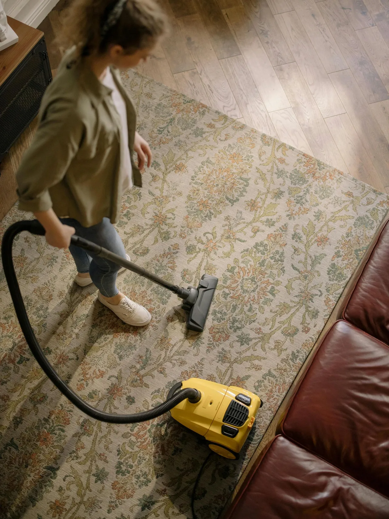 A woman is using a vacuum cleaner to clean a rug in a living room.