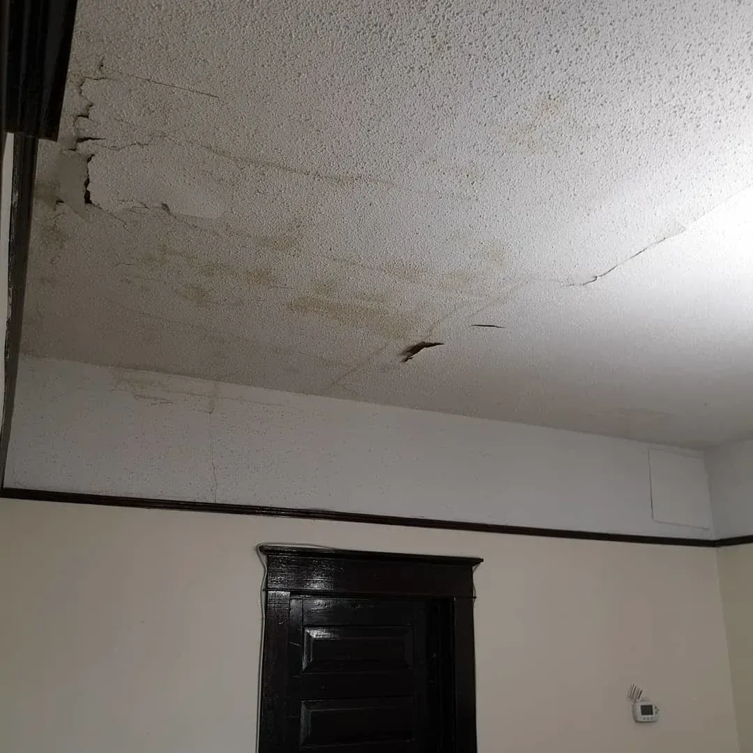 water damage on the ceiling above a dark doorway in a plain room