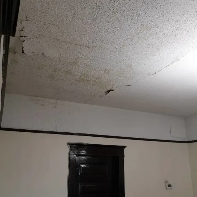 water damage on the ceiling above a dark doorway in a plain room